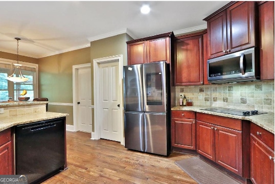 kitchen with light wood-type flooring, black appliances, light stone countertops, decorative backsplash, and decorative light fixtures