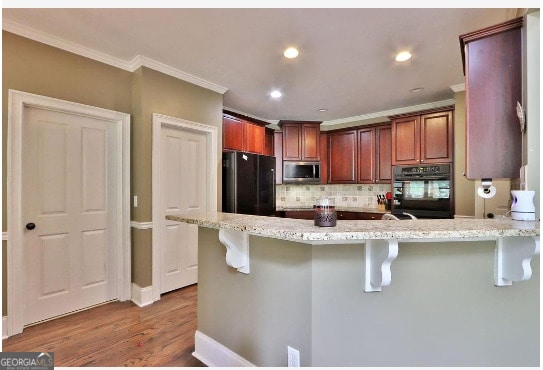 kitchen featuring decorative backsplash, wood-type flooring, black appliances, and a breakfast bar