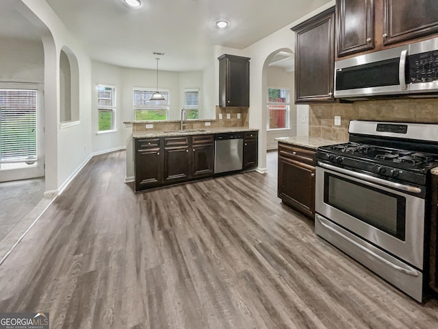 kitchen with decorative light fixtures, sink, dark brown cabinetry, stainless steel appliances, and light stone countertops