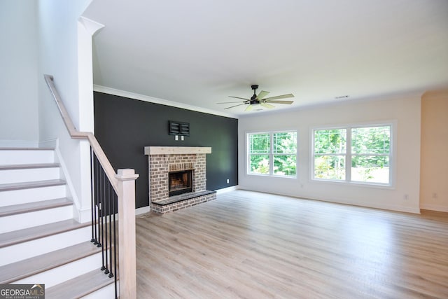 unfurnished living room with ceiling fan, a brick fireplace, ornamental molding, and light wood-type flooring