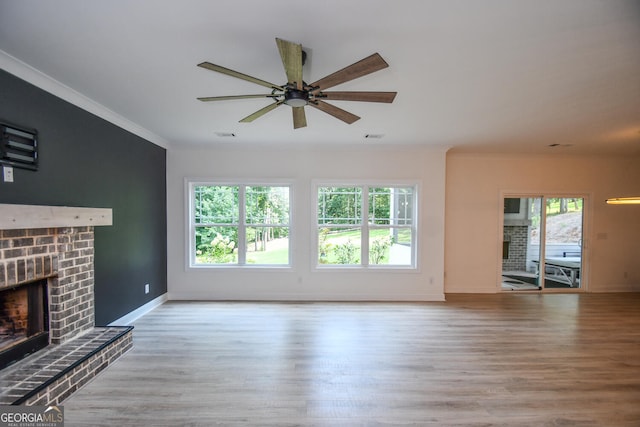 unfurnished living room featuring ornamental molding, a brick fireplace, ceiling fan, and light wood-type flooring