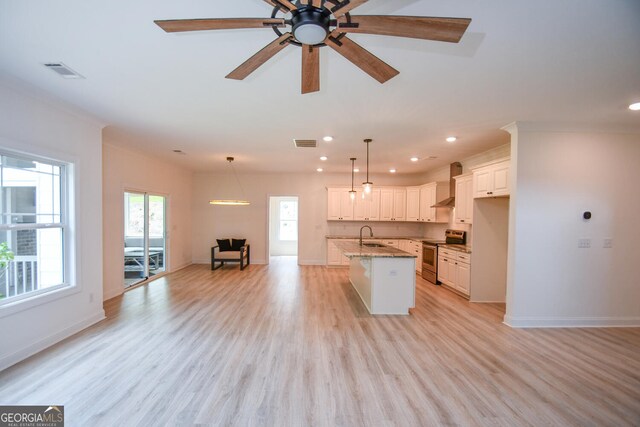 kitchen featuring electric range, light hardwood / wood-style flooring, wall chimney range hood, light stone counters, and a center island with sink