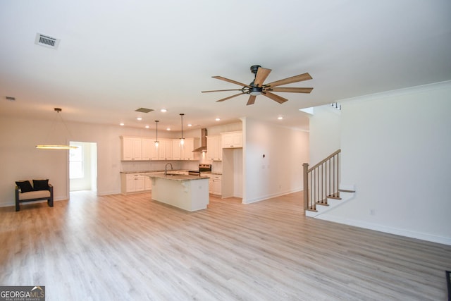 kitchen featuring decorative light fixtures, white cabinetry, a kitchen island with sink, wall chimney exhaust hood, and electric stove