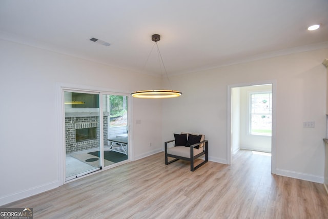 living area featuring crown molding, light hardwood / wood-style floors, and a brick fireplace
