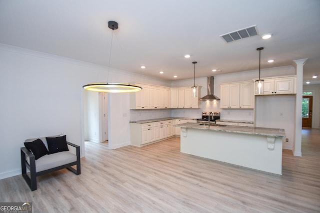 kitchen featuring wall chimney exhaust hood, sink, light stone counters, an island with sink, and pendant lighting