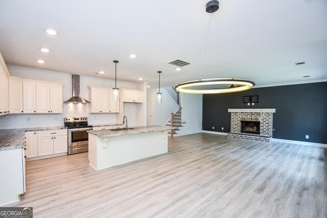 kitchen with a fireplace, pendant lighting, light wood-type flooring, wall chimney exhaust hood, and stainless steel range with electric cooktop