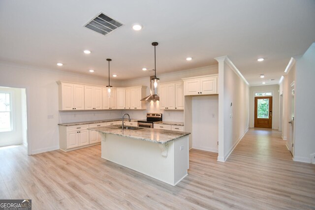 kitchen featuring light hardwood / wood-style flooring, wall chimney range hood, light stone counters, electric stove, and a center island with sink