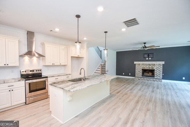 kitchen featuring wall chimney range hood, a fireplace, sink, light hardwood / wood-style floors, and electric range