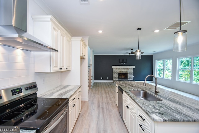 kitchen featuring appliances with stainless steel finishes, decorative light fixtures, sink, light stone counters, and wall chimney exhaust hood