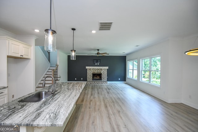 kitchen with sink, light stone counters, hanging light fixtures, light hardwood / wood-style flooring, and a fireplace