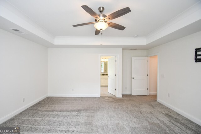 unfurnished bedroom featuring ceiling fan, ensuite bath, crown molding, light colored carpet, and a raised ceiling