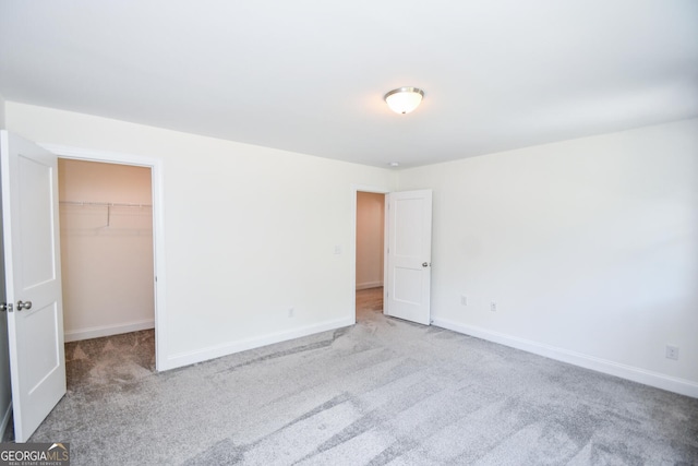 unfurnished bedroom with a walk in closet, a closet, and light carpet