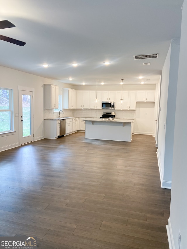 kitchen with appliances with stainless steel finishes, pendant lighting, white cabinets, hardwood / wood-style floors, and a kitchen island