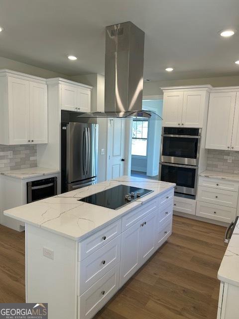 kitchen with island exhaust hood, a center island, stainless steel appliances, and white cabinets