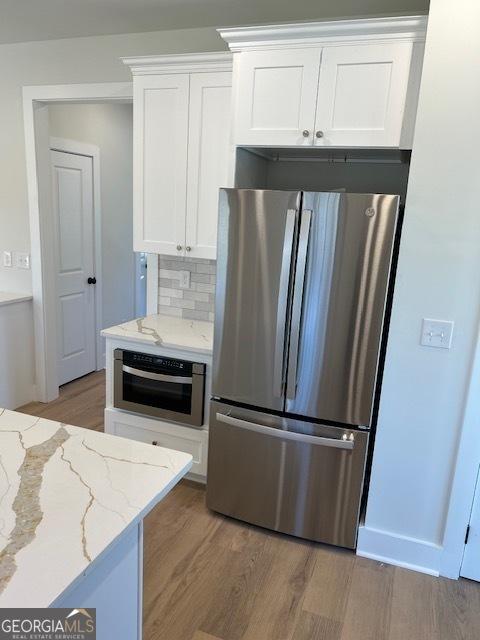 kitchen featuring stainless steel appliances, light stone counters, light hardwood / wood-style flooring, decorative backsplash, and white cabinets