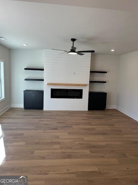 unfurnished living room with ceiling fan, a fireplace, and wood-type flooring