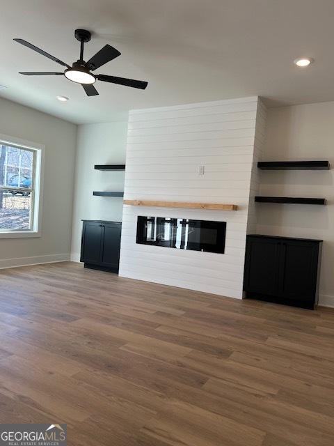 unfurnished living room featuring hardwood / wood-style floors, ceiling fan, and a large fireplace