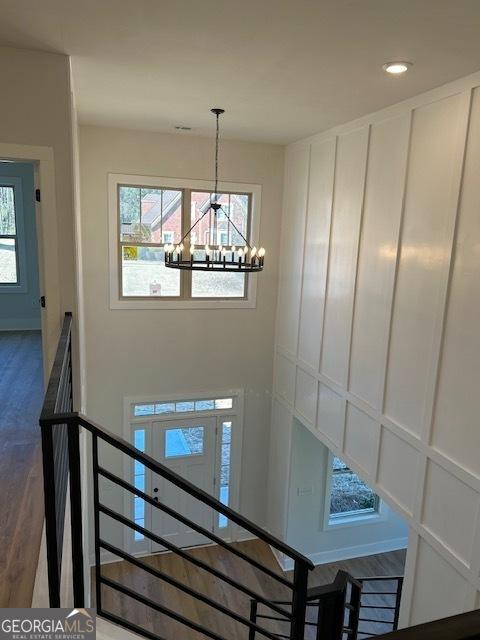 stairs featuring a healthy amount of sunlight, wood-type flooring, and an inviting chandelier