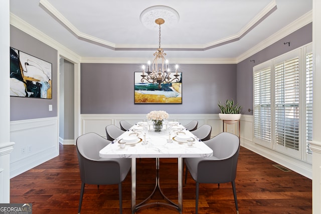 dining room featuring a raised ceiling, dark wood-type flooring, an inviting chandelier, and crown molding