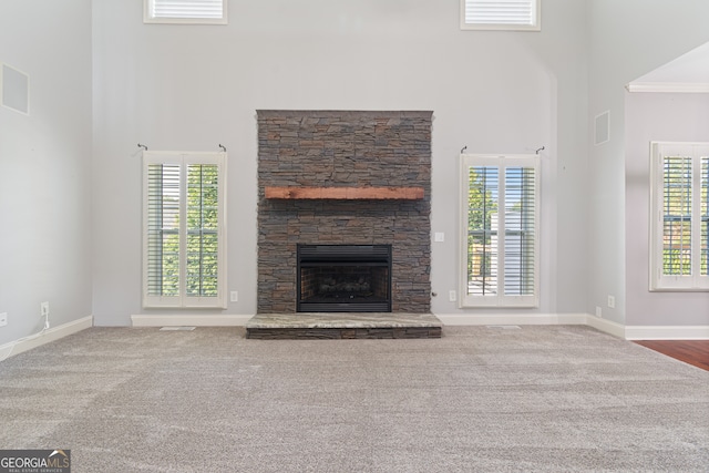 unfurnished living room with crown molding, a wealth of natural light, a stone fireplace, and carpet floors