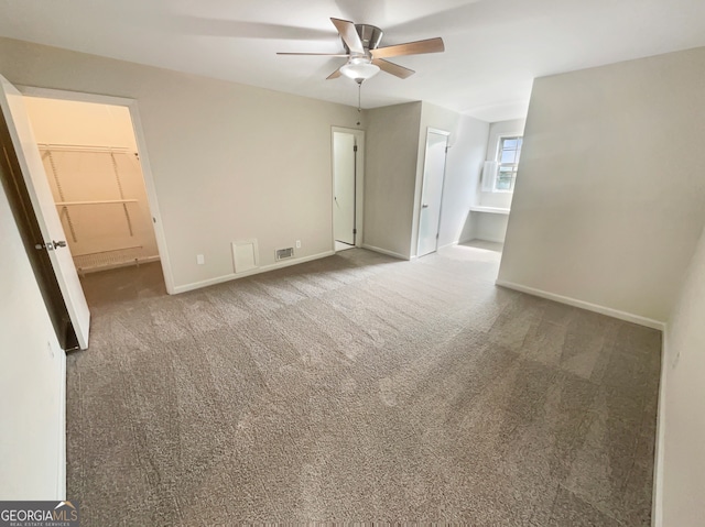 unfurnished bedroom with a spacious closet, a closet, connected bathroom, carpet flooring, and ceiling fan