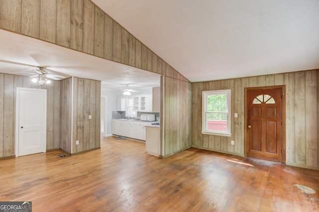 foyer entrance featuring light hardwood / wood-style floors, wood walls, vaulted ceiling, and ceiling fan