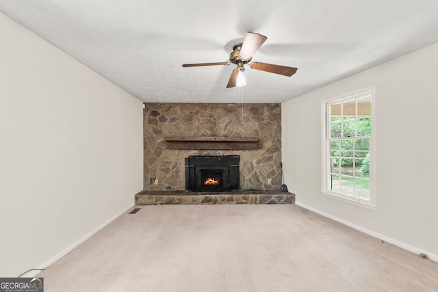 unfurnished living room with a stone fireplace, a textured ceiling, ceiling fan, and carpet flooring