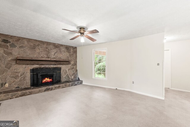 unfurnished living room with light carpet, a textured ceiling, a stone fireplace, and ceiling fan