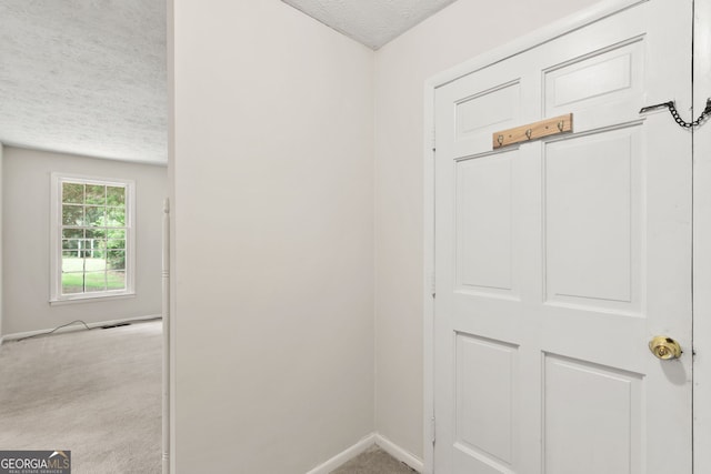 hall with light carpet and a textured ceiling