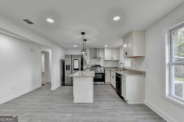 kitchen featuring appliances with stainless steel finishes, light hardwood / wood-style flooring, a center island, and wall chimney range hood