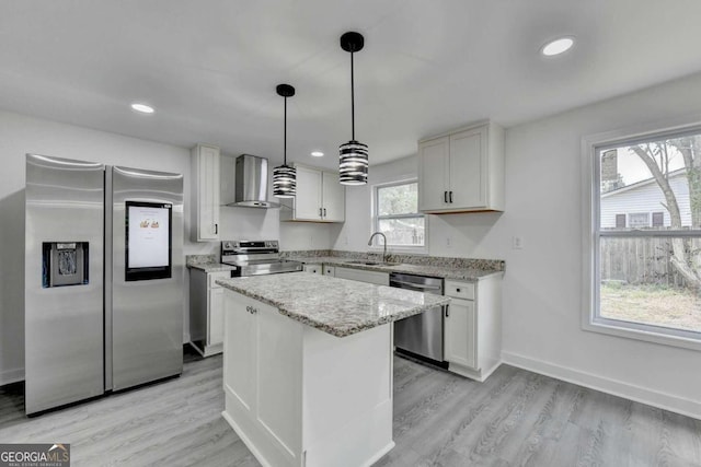 kitchen with appliances with stainless steel finishes, light wood-type flooring, wall chimney range hood, and a kitchen island