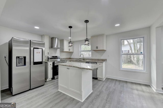 kitchen featuring appliances with stainless steel finishes, white cabinetry, light wood-type flooring, and wall chimney range hood