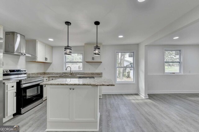 kitchen with a healthy amount of sunlight, wall chimney exhaust hood, range with electric cooktop, and light hardwood / wood-style floors