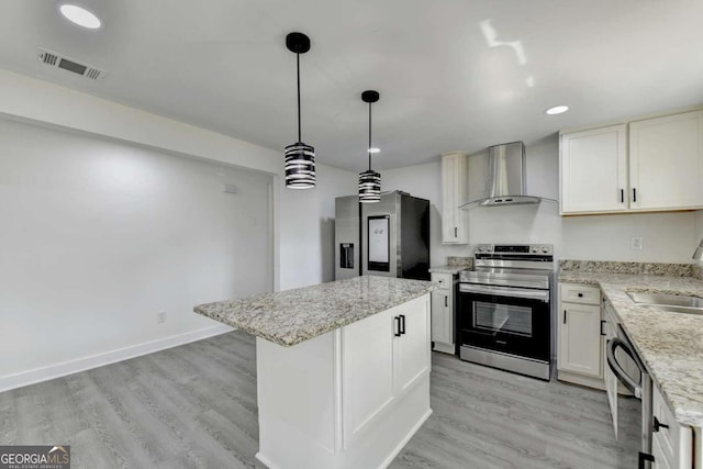 kitchen featuring light hardwood / wood-style flooring, wall chimney range hood, a kitchen island, stainless steel appliances, and decorative light fixtures