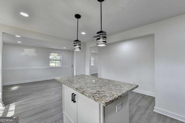 kitchen with light hardwood / wood-style flooring, white cabinets, light stone counters, a kitchen island, and decorative light fixtures