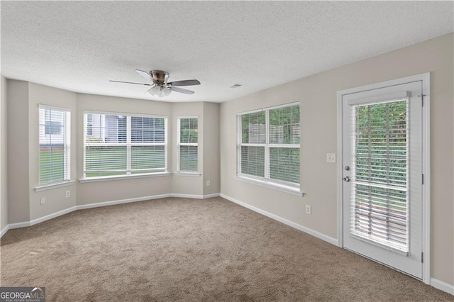 spare room with a textured ceiling, carpet flooring, a wealth of natural light, and ceiling fan