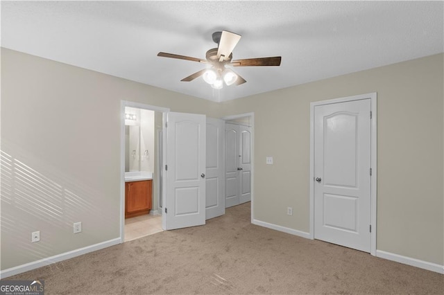 unfurnished bedroom with light carpet, ensuite bathroom, and ceiling fan