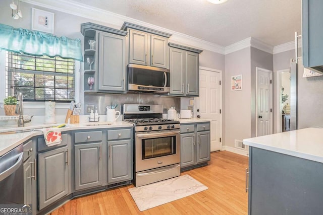 kitchen with ornamental molding, gray cabinetry, appliances with stainless steel finishes, and light hardwood / wood-style floors