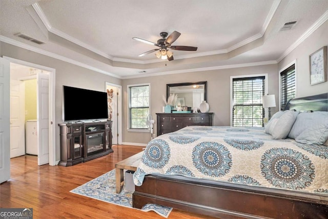 bedroom with a textured ceiling, a raised ceiling, crown molding, hardwood / wood-style flooring, and ceiling fan