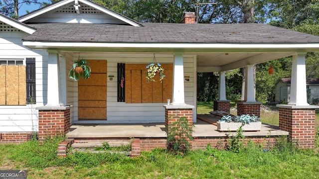 doorway to property featuring a shingled roof, covered porch, and a chimney