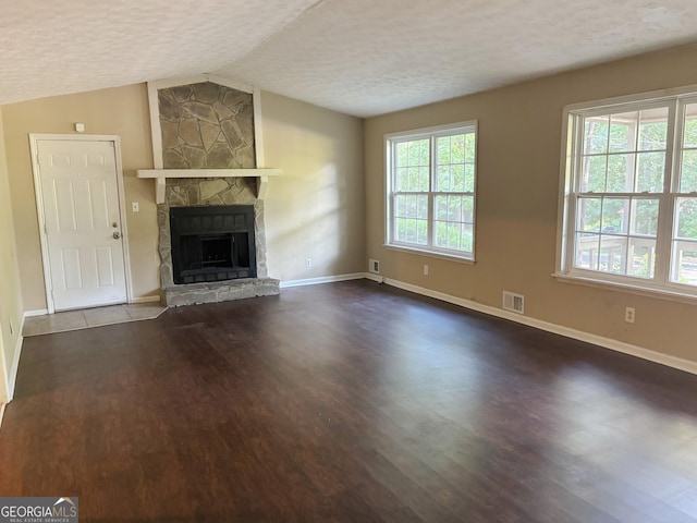 unfurnished living room with a textured ceiling, lofted ceiling, a stone fireplace, and wood-type flooring