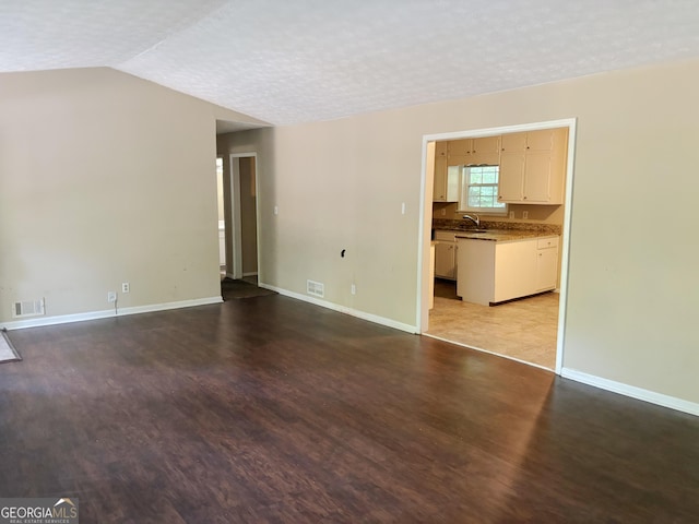 unfurnished living room with sink, light wood-type flooring, a textured ceiling, and lofted ceiling