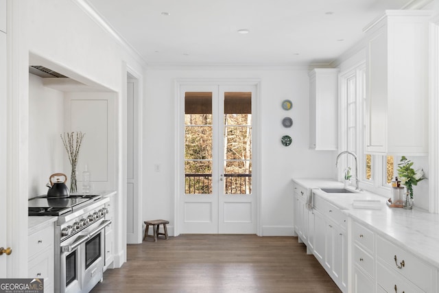 kitchen featuring light stone countertops, white cabinets, range with two ovens, light hardwood / wood-style floors, and sink