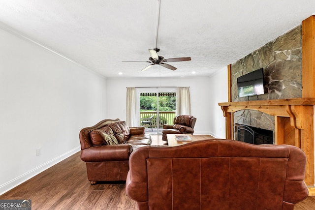 living room featuring hardwood / wood-style flooring, ceiling fan, a stone fireplace, and a textured ceiling