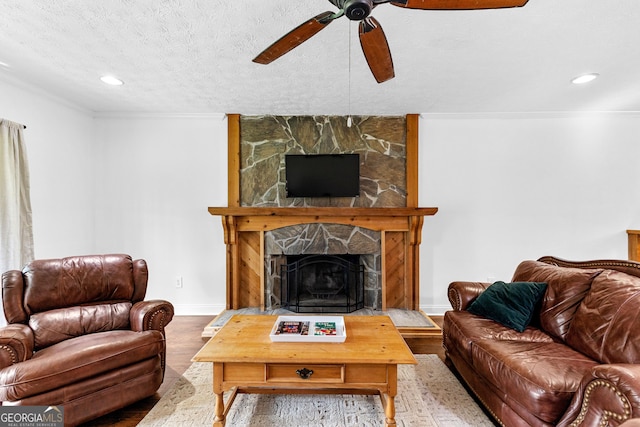 living room with a stone fireplace, a textured ceiling, ornamental molding, hardwood / wood-style flooring, and ceiling fan