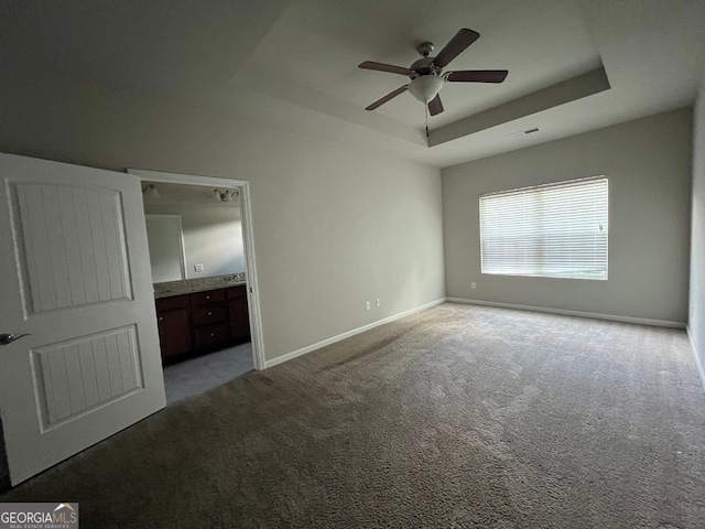 unfurnished bedroom with light carpet, ceiling fan, a raised ceiling, and connected bathroom