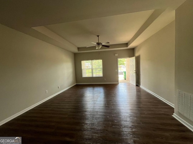 empty room with ceiling fan, dark hardwood / wood-style floors, and a tray ceiling