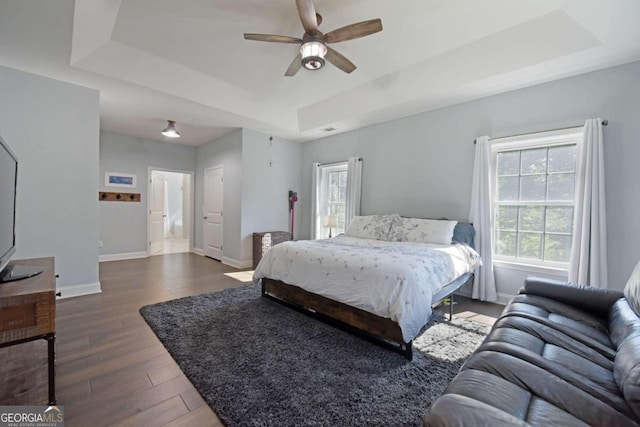 bedroom with ceiling fan, dark hardwood / wood-style flooring, and a tray ceiling