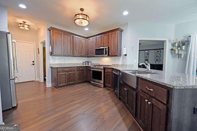 kitchen with stainless steel appliances, kitchen peninsula, decorative backsplash, light stone countertops, and wood-type flooring