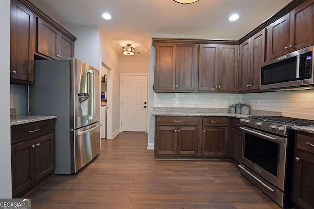 kitchen with appliances with stainless steel finishes, dark hardwood / wood-style flooring, decorative backsplash, and light stone countertops